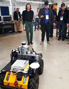 mobile robot in foreground as UT researcher shows DOD visitor how to move it